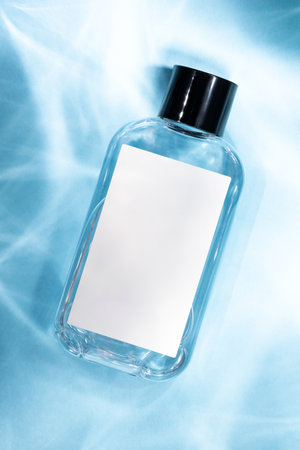 A cosmetic glass bottle with a blank white label on a pastel blue background. Perfect for showcasing...