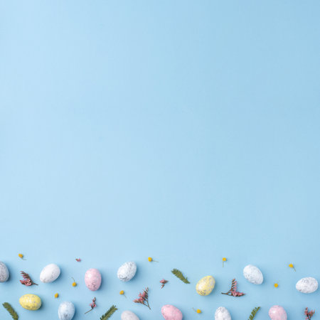 Festive Easter background. Multicolored Easter eggs and flowers on a blue table. Card with a place for text. Top view.の写真素材