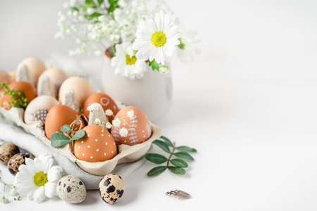 A delicate Easter background with hand-painted eggs in a box on a white table. Easter composition with flowers and feathersの写真素材