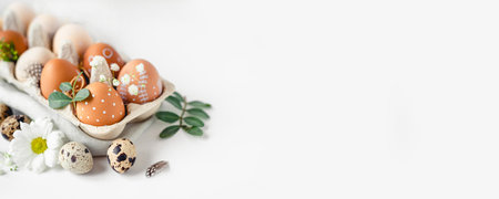 A delicate Easter background with hand-painted eggs in a box on a white table. Easter composition with flowers and feathersの写真素材