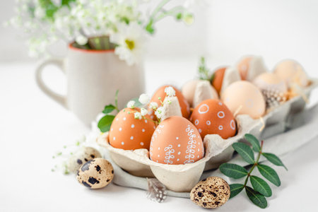 A delicate Easter background with hand-painted eggs in a box on a white table. Easter composition with flowers and feathersの写真素材