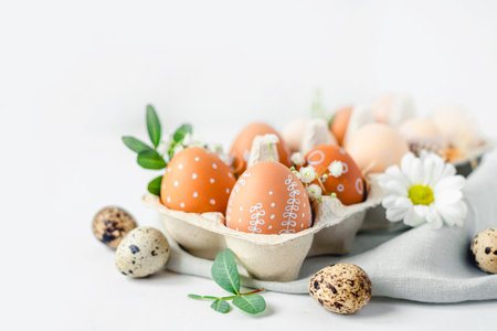 A delicate Easter background with hand-painted eggs in a box on a white table. Easter composition with flowers and feathersの写真素材