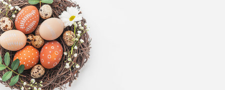 Easter nest with hand-painted eggs and quail eggs on a light background. A rustic spring composition with natural elements, fresh greenery and floral details.の写真素材