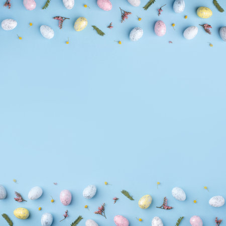 Festive Easter background. Multicolored Easter eggs and flowers on a blue table. Card with a place for text. Top view.の写真素材