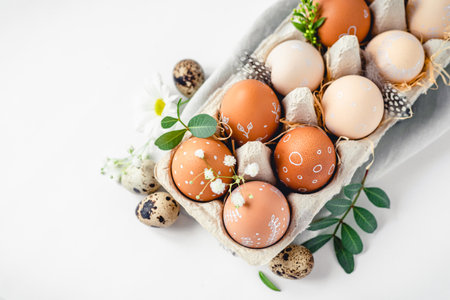A delicate Easter background with hand-painted eggs in a box on a white table. Easter composition with flowers and feathersの写真素材