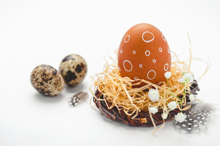 Easter nest with hand-painted egg and quail eggs on a light background. A rustic spring composition with natural elements, fresh greenery and floral details.の写真素材