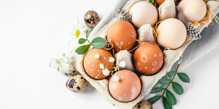 A delicate Easter background with hand-painted eggs in a box on a white table. Easter composition with flowers and feathersの写真素材