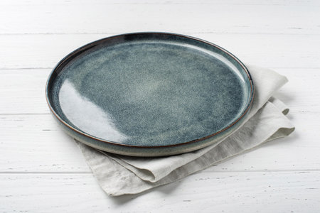 An empty gray textured plate with a napkin on a white wooden tableの写真素材