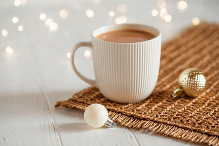 A white cup with hot coffee or tea on a white wooden table with Christmas lights.の写真素材