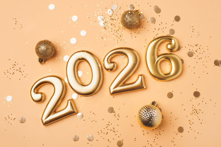 Golden 2026 on a peach color background with confetti and bokeh lights. Happy New Year 2026 is...