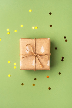 A Christmas gift wrapped in eco-friendly packaging on a green background with golden confettiの写真素材