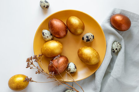 Golden and bronze Easter eggs in a orange plate on a linen napkin on a white backgroundの写真素材