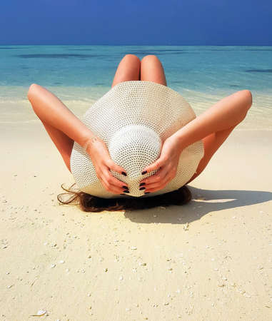 Girl holding hat laying on the sand watching to the sea