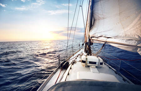View from the deck to the bow of a sail yacht tilted in a wind on a sunset. Seen reefed sails, mast and boom. Strong wind before the storm.の写真素材