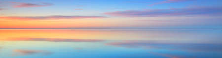 Picturesque panoramic scenery of the open Baltic sea at sunset. Symmetry reflections on the water, natural mirror. Breathtaking view. Winter seascape. Pure nature, seasons, climate changeの写真素材