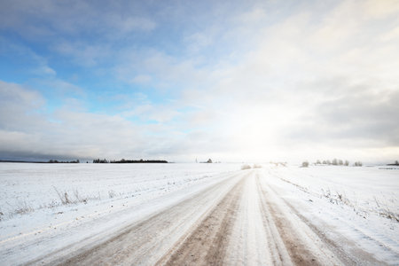 Snow-covered country road through the fields after a blizzard at sunset. Old rustic house in the background. Winter rural scene. Dramatic sky, colorful cloudscape. Ice desert. Lapland, Finlandの写真素材