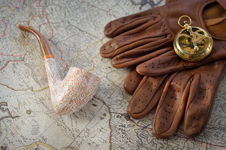 Retro style golden compass (sundial), elegant smoking pipe, brown leather gloves, lighter and accessories, old white nautical chart close-up. Vintage still life. Travel gentleman setの写真素材