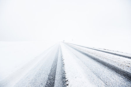 Snow-covered highway (asphalt road) through the country fields in a fog after a blizzard. Dangerous driving, climate change, global warming, ecology, environmental conservationの写真素材