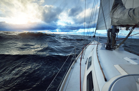 Yacht sailing in an open sea on a winter day. Close-up view from the deck to the bow, mast and sails. Dramatic stormy sky, dark clouds. Epic seascape. North sea, Norwayの写真素材