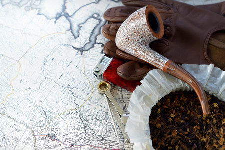 Elegant smoking pipe, tobacco, lighter, accessories, brown leather gloves, old white nautical chart close-up. Vintage still life. Travel gentleman set. Planning travel, sailing, adventure, concept artの写真素材