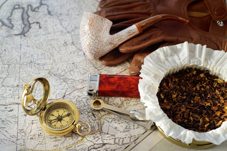 Retro style golden compass (sundial), elegant smoking pipe, brown leather gloves, lighter and accessories, old white nautical chart close-up. Vintage still life. Travel gentleman setの写真素材