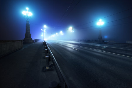 Pedestrian walkway and highway through the illuminated empty Stone bridge in a thick fog at night. Lanterns close-up. Daugava river, Riga, Latvia. Concept image, neon colorsの写真素材