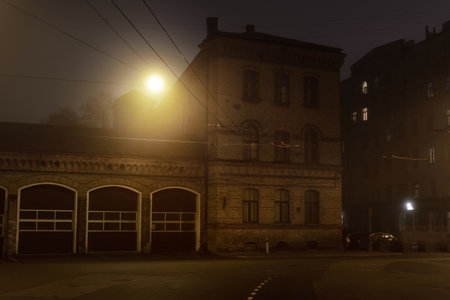 An empty illuminated asphalt road through the old historical buildings and houses in a fog at night. Street lights (lanterns) close-up. Riga, Latvia. Dark cityscapeの写真素材