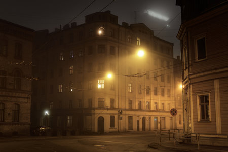 An empty illuminated asphalt road through the old historical buildings and houses in a fog at night. Street lights (lanterns) close-up. Riga, Latvia. Dark cityscapeの写真素材