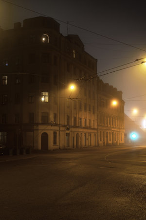 An empty illuminated asphalt road through the old historical buildings and houses in a fog at night. Street lights (lanterns) close-up. Riga, Latvia. Dark cityscapeの写真素材