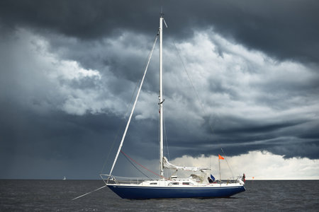 Blue sloop rigged yacht anchored off the coast of England under the dark sky after a thunderstorm....