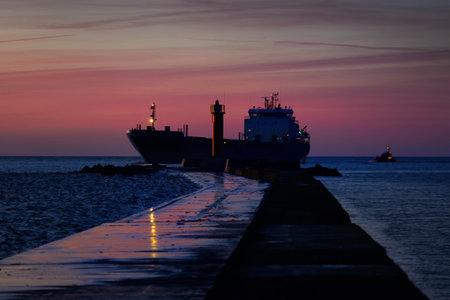 Large cargo ship sailing near the lighthouse at sunset. Colorful cloudscape. Riga bay, Baltic sea, Latvia. International communications, logistics themeの写真素材