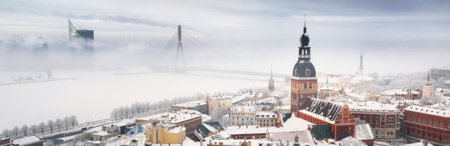 Panoramic aerial view of the Riga old town and Daugava river from St. Peter's Church in winter. Morning fog, snow-covered cable-stayed bridge, cathedral, houses. Latvia. Landmarks, sightseeing, travelの写真素材