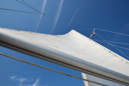 White yacht sails against clear blue sky with cirrus clouds and plane tracks, close-up. Ruhnu island, Estonia, Baltic seaの写真素材