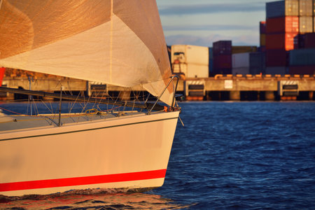 White yacht sailing in Daugava river at sunset, close-up. Cargo containers in the background. Riga bay, Latviaの写真素材
