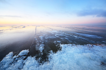 Panoramic view of the snow-covered shore of the frozen Saima lake at sunset. Ice fragments close-up. Colorful cloudscape. Symmetry reflections on the water. Finlandの写真素材