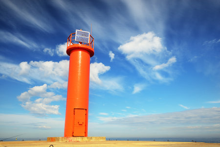 Low angle view of the orange lighthouse with a solar battery against clear blue sky with cirrus clouds. Dramatic cloudscape. Riga bay, Baltic sea, Latvia. Alternative energy. ecology, sightseeingの写真素材