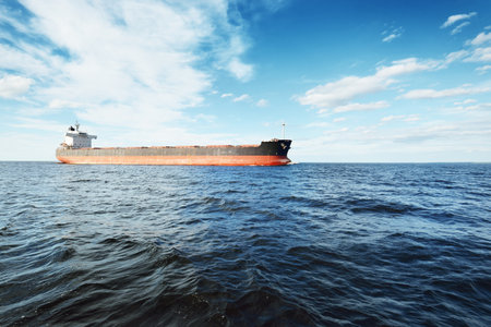 Large bulk carrier (cargo ship) sailing in an open sea from Europoort. Clear blue sky with cirrus clouds. Rotterdam, Netherlands. Global communications, logistics, industry themeの写真素材
