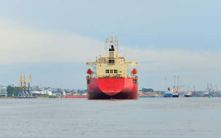 Large red bulk carrier (cargo ship) with a cranes arriving to the Europoort, close-up. Rotterdam, Netherlands. Freight transportation, global communications, logistics, industry themeの写真素材