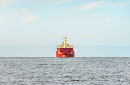 Large red bulk carrier (cargo ship) with a cranes sailing in an open sea from Europoort. Clear blue sky with cirrus clouds. Rotterdam, Netherlands. Global communications, logistics, industry themeの写真素材