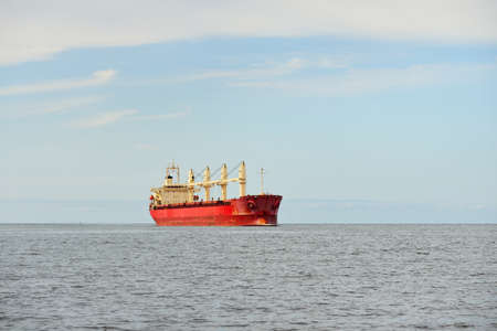Large red bulk carrier (cargo ship) with a cranes sailing in an open sea from Europoort. Clear blue...