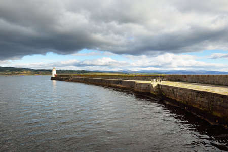 An empty promenade to the old lighthouse, close-up. Rocky shores in the background. Dramatic cloudscape. Ardrishaig, Crinan canal, Scotland, UKの写真素材