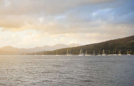 Stunning sunset cloudscape. Sloop rigged yachts and wooden boats anchored on mooring near the shore...
