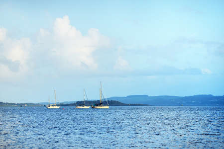 Yachts and wooden boats anchored on mooring near the shore of Gare Loch and a small village Rhu,...