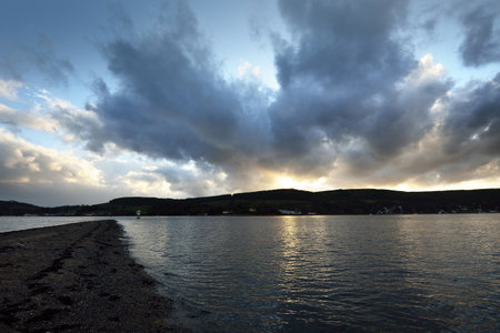 Rocky lake shores and lighthouse under the colorful evening sky after the rain. Dramatic cloudscape. Gare Loch, Rhu, Scotland, UKの写真素材