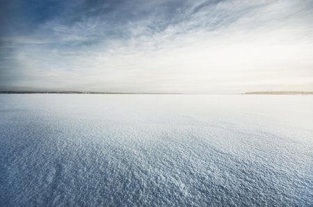 Frozen snow-covered lake under a clear blue sky with cirrus clouds. Fresh snow texture. Arctic, Lapland. Global warming, winter sport and fishing, environmental conservation themeの写真素材