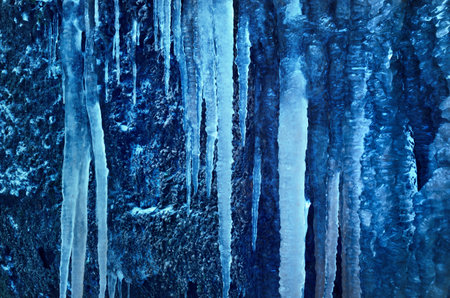 Large blue icicles close-up, cliff in the background. Frozen water, ice texture. Abstract art, natural pattern. Graphic resources, backgrounds, environmental conservation, climate change themeの写真素材