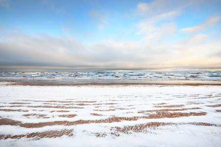 A view from the snow-covered Baltic sea shore at sunset. Riga bay, Latvia. Colorful dramatic cloudscape. Fickle weather, waves and water splashes. Winter tourism, global warming themeの写真素材