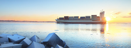 Large cargo container ship sailing against sunset sky. Riga bay, Baltic sea, Latvia. Freight transportation, global communications, logistics, industry, business, economy, environmental damageの写真素材