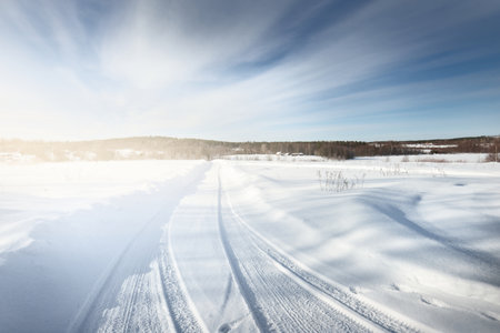 An empty country road with a sharp turn through the snow-covered field after a blizzard. Dramatic sky with glowing clouds. Karelia, Russia. Road trip, eco tourism, environmental conservation conceptsの写真素材