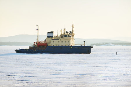 A man standing in front of an icebreaker. Frozen lake at sunset. Concept winter landscape. White Sea, Polar Circle, Russia. Ice texture. Expedition, work, research, Arctic shipping routes, logisticsの写真素材